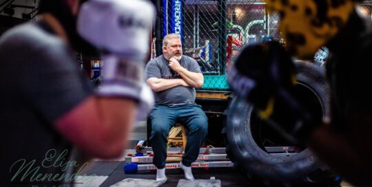 Joe sitting and watching fighters workout in his gym.