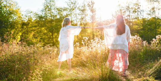 Dawn Michelle and Hadley standing in a field, reaching for each other.